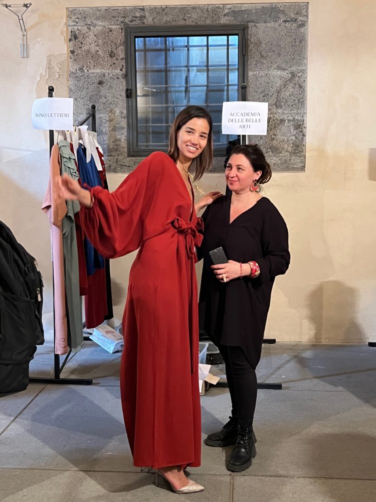 A red silk dress with an overlapping skirt and puffed sleeves are worn by this model for EVALab, photographed during the fitting for the fashion show at Napoli Moda Design together with Professor Maddalena Marciano of the Academy of Fine Arts in Naples.